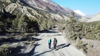 一对夫妇在尼泊尔喜马拉雅山脉的马南谷的一条森林小径上散步。安纳普尔纳的尖峰和贫瘠的山峰在后面。安纳普尔纳峰电路长途跋涉。大自然的美。尘土飞扬的道路。视频素材模板下载