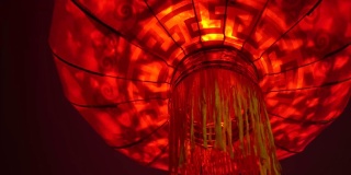 一个红色圆灯笼的特写，里面有一个灯泡，在中国新年庆祝期间的晚上在风中摇摆