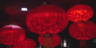 一个红色圆灯笼的特写，里面有一个灯泡，在中国新年庆祝期间的晚上在风中摇摆