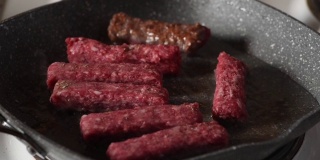 男人用叉子把鲜红的烤肉串放在煎锅里，用热油煎它们，在家庭厨房里近距离选择性聚焦食物概念
