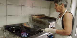 一名妇女在商业厨房的煎锅里准备撒上面包屑的鸡肉