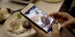 一名年轻的亚洲女子用手机在桌上给冰淇淋布朗尼拍照。