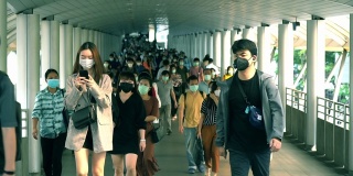 在泰国曼谷的崇诺寺BTS车站，下班高峰期，许多人戴着面具走在大桥上的慢镜头。