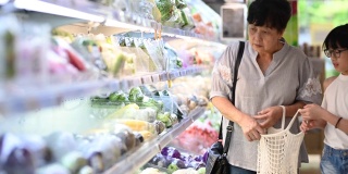 一位亚洲华人的祖母和孙女在杂货店的冰箱蔬菜区挑选和购买蔬菜