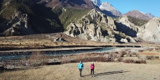 一对夫妇进入尼泊尔喜马拉雅山脉的马南谷。他们走在一条干燥、尘土飞扬的路上，走向一条小溪。高山环绕着他们。旁边的小屋。探索和冒险。