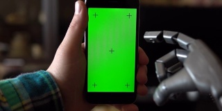 电子人使用电话。一只灰色的机械手正按在绿色屏幕的智能手机上。色度键。4 k