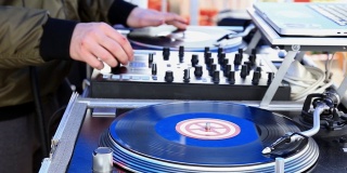 DJ播放音乐，在一个转盘上刮黑胶唱片在露天派对。手的特写镜头。