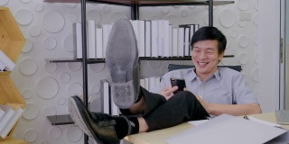 亚洲高级男子正坐在办公室里看着屏幕手机工作着，笑着开心的脸笑着开心的成功