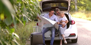 快乐的小家庭坐在汽车的敞篷后备箱里看着地图