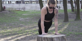 健康的女人在树林里锻炼在公园的木头上做俯卧撑。在户外自然健身房锻炼，做俯卧撑。迷人的女运动员在公园里锻炼，做俯卧撑。在户外运动