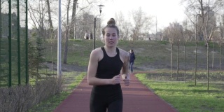 年轻女子在公园的跑道上慢跑。活动的人。跑步者在跑道上跑步。保持身体健康。有橡皮筋覆盖的跑道，用于行走和赛跑