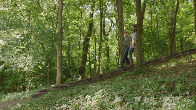 慢动作拍摄的一个白人男人和女人在他们的四十多岁一起走下山的森林在一个阳光明媚的一天在田纳西州