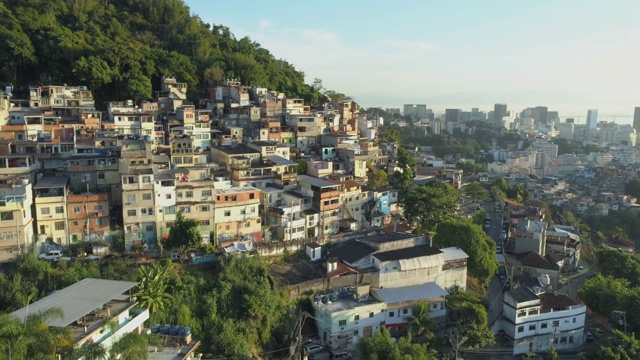 日出在空中飞过森林下的山顶贫民窟，背景是市中心的高楼大厦