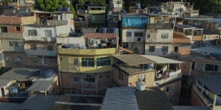 日出时，巴西里约热内卢，空中追踪经过山顶上树木之间密集的贫民窟住宅