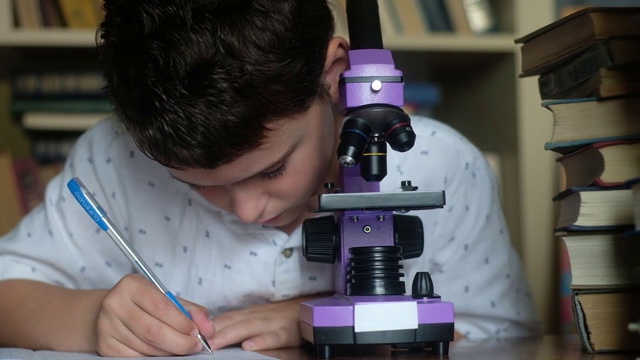 男孩看着紫色的显微镜，扭曲透镜，在笔记本上写下溶液。