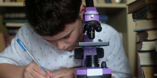 男孩看着紫色的显微镜，扭曲透镜，在笔记本上写下溶液。