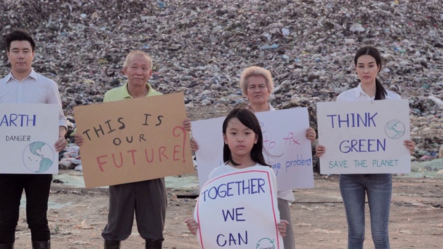 五名不同年龄的志愿者站在亚洲一个巨大的垃圾填埋场，手持环保运动人士为大自然而战的海报。志愿服务、慈善、清洁、家庭、生态理念