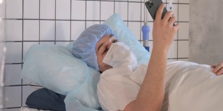 男病人在医院病床上休息时拿着手机