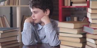 一个男生睡在桌子上。在学校的一堆书中叫醒一个孩子。