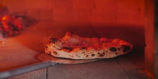 Checks pizza for readiness by pulling it out of the pizza oven using the pizza rind.