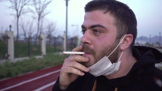 一个戴着面具的年轻人在公园里抽烟视频素材模板下载