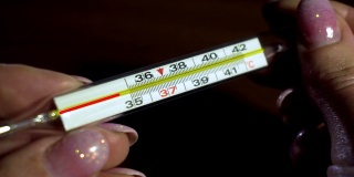 在世界范围内死亡病毒流行期间，妇女手上的玻璃医用温度计用动画显示温度上升到37摄氏度