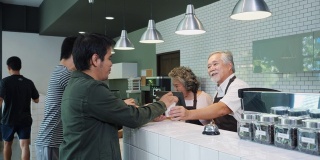 亚洲男服务员在咖啡馆餐厅与顾客交谈。商人工作和接受订单的女顾客进入咖啡店与快乐美好的一天。业主经营咖啡馆的理念。