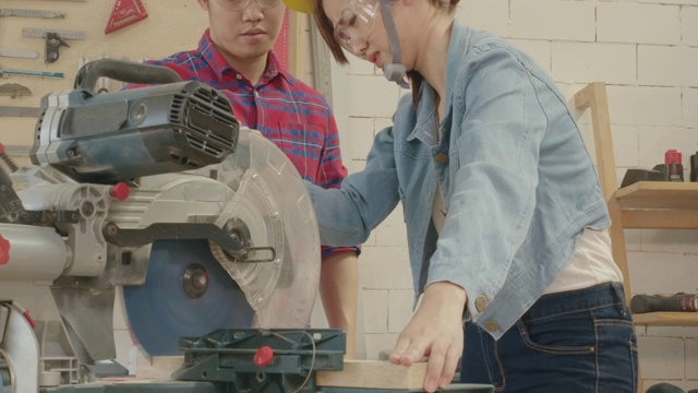 培训木工指导木工培训生在工业车间办公室使用切割机，男木匠监督女学徒学习安全之间的工作理念。