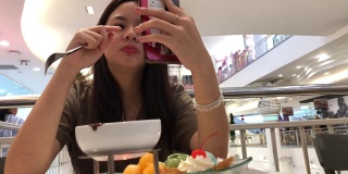 亚洲少女一边在咖啡店吃冰淇淋，一边用智能手机进行网络摄像头，身体状况良好，竖起大拇指