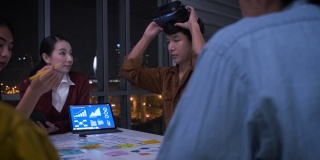 亚洲用户体验开发人员和ui设计师在夜晚的城市灯光下，在现代办公室中使用手机应用原型设计虚拟现实眼镜。创意数字发展机构