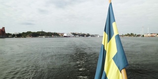 瑞典国旗在风中飘扬的船尾馈水旗杆在斯德哥尔摩城市中心港口航行