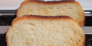 在粉红色的背景下，烤面包从白色的烤面包机里跳出来，特写