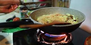 一个亚洲中国女性在家里烹饪中餐炒面在炉灶上烹饪平底锅