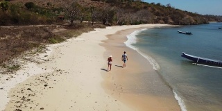 一对情侣在龙目岛的粉色沙滩上散步。这个地方是一块隐藏的宝石，不会被游客破坏。孤独和平静的感觉，海浪轻轻在沙滩上蔓延。岸边有许多五颜六色的船