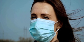 慢镜头悲伤的女子戴着医用口罩，蓝天下呼吸新鲜空气，为抗击冠状病毒而奋战