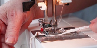 近距离观察缝纫过程。在新冠肺炎大流行期间，女性双手在缝纫机上用棉织品缝制医用口罩