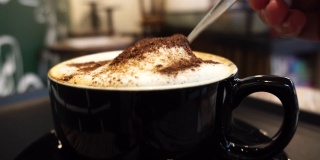 用勺子混合巧克力粉和奶泡在咖啡卡布奇诺上
