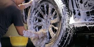 洗车和细化。一名专业工人正在洗车厂用肥皂泡沫洗车。汽车修理厂的工人正在清洗车轮