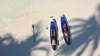 一对年轻夫妇躺在桨板上，在棕榈树的树荫下视频素材模板下载