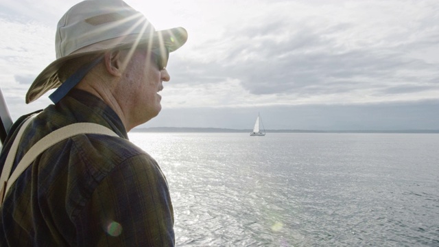 一名六十多岁的男子在多云的一天从一艘帆船的甲板上俯瞰华盛顿普吉特海湾的慢动作镜头