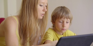 一位年轻妇女和她的小儿子在隔离期间坐在家里，在互联网学校使用平板电脑学习。冠状病毒的概念