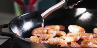 厨师将橄榄油倒在煎锅里的虾上，慢动作。大虾在平底锅里煎。