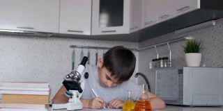 这个男孩用显微镜和装有液体的瓶子学习生物，并在笔记本上做笔记。家庭作业