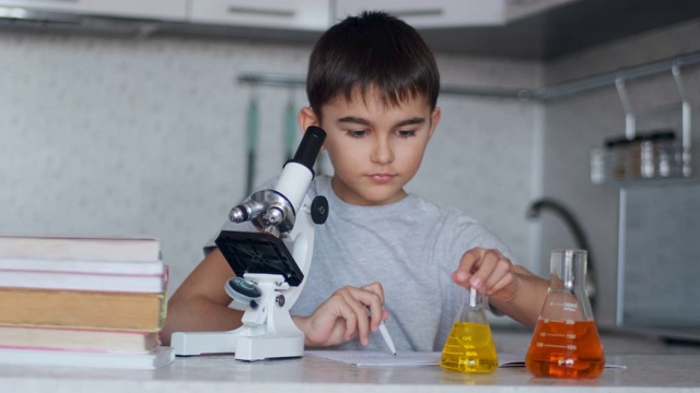 特写镜头。这个男孩用显微镜和盛有液体的瓶子教化学，并在笔记本上做笔记。家庭作业