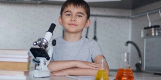 一个聪明的学生坐在家里的桌子旁边，旁边是一个显微镜和装有液体的瓶子