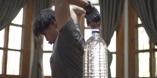 一名男子在家用塑料瓶装水而不是健身房的哑铃锻炼他的肱三头肌