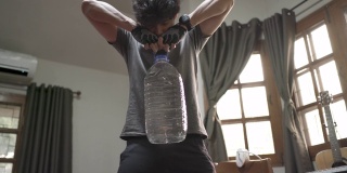 亚洲男人在家里锻炼举起塑料加仑水瓶