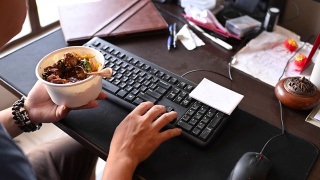一个亚洲华人中年男子正在吃午餐，在他的家庭办公室工作的时候吃他的午餐视频素材模板下载