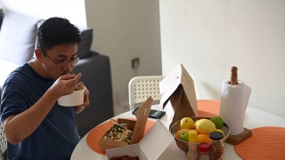 一名亚洲华人中年男子用手机拍下他点的外卖放在餐桌上视频素材模板下载