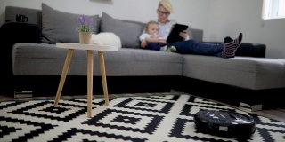 女人和男孩在用平板电脑，机器人在用吸尘器清扫家里的地板。现代生活方式的概念。